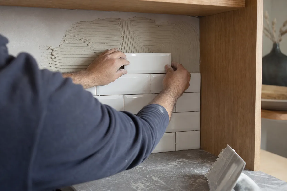 Pose de faïence murale format métro sur une crédence de cuisine, mains positionnant un carreau
